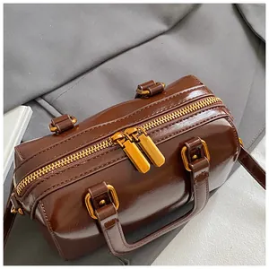 Detail of brown shiny Boston bag with double gold zippers and smooth leather texture