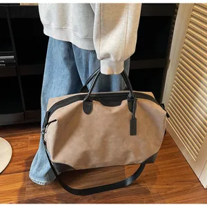 Large khaki travel tote bag with black handles held in a stylish indoor lifestyle setting.