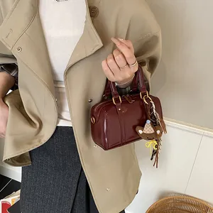 Stylish burgundy mini Boston bag with bear charm shown in a chic lifestyle setting