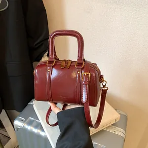 Elegant burgundy glossy leather Boston bag with gold hardware and dual top handles.