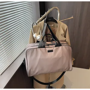 Large mauve travel bag hanging on a garment rack with a beige trench coat and headphones