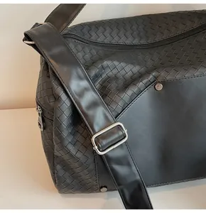 Dettaglio della borsa da viaggio intrecciata nera con tracolla regolabile e fibbia argento.