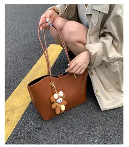 Gros plan d'un grand sac cabas en cuir marron avec un porte-clés ours en peluche mignon.