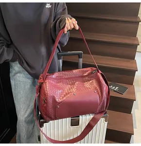Dettaglio ravvicinato di una grande borsa da viaggio intrecciata bordeaux su una valigia