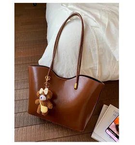 Gros plan d'un grand sac cabas en simili cuir marron avec un pendentif ours en peluche