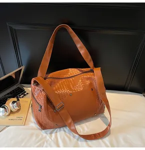 Dettaglio di una grande borsa da viaggio intrecciata marrone su un letto con vari oggetti