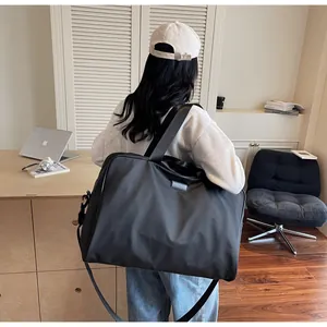 Black large capacity travel duffle bag carried by a person in a minimalist room setting.