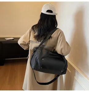 Borsa da viaggio intrecciata nera indossata sulla spalla su un trench beige