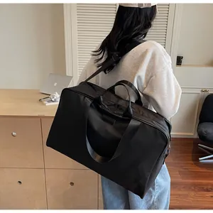 Large black duffel bag with shoulder strap carried by a woman in a minimalist room.