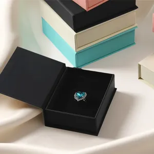 Detalle de un joyero magnético negro abierto con un anillo de corazón azul adentro.