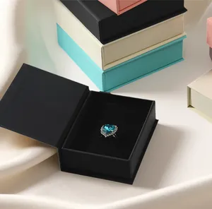 Primer plano de un estuche de joyería magnético tipo libro negro con un anillo de corazón