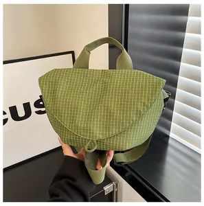 Vista detallada de un bolso bandolera de lona a cuadros verdes con cierre magnético.