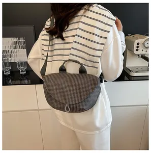 Vista detallada de un bolso bandolera gris con patrón de rejilla usado por una modelo.