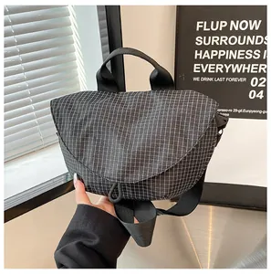 Vista detallada del bolso bandolera de lona con diseño a cuadros negros y una asa
