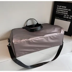 Large grey metallic travel duffel bag with black straps shown in a minimalist room setting