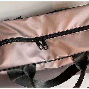 Detailed close-up showing the smooth satin fabric and black double zipper of a pink travel bag.