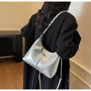 Close-up of a silver metallic shoulder bag with a chain strap worn over a black coat