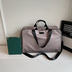 Large taupe travel duffel bag for women shown with tablet for size reference in a room.