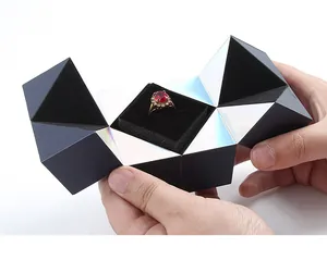 Caja para anillo de cubo mágico abierta con un anillo de rubí rojo en la mano.