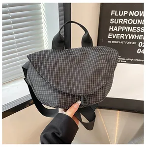 Detalle del bolso bandolera de lona con patrón de cuadrícula negra y cierre magnético.