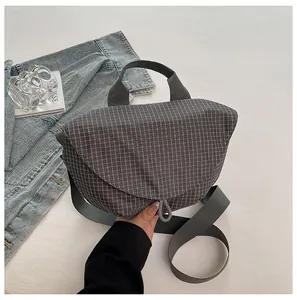 Vista detallada de un bolso bandolera gris a cuadros con cierre magnético y correa ancha.
