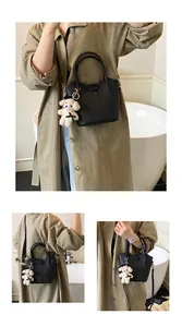 Chic black bucket handbag with bear charm shown in crossbody and handheld poses.