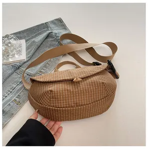 Vista detallada de un bolso bandolera de lona con patrón de cuadros marrones y cierre imán