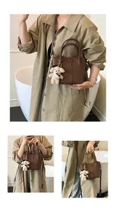 Fashionable brown leather bucket handbag for women featuring a cute teddy bear charm accessory