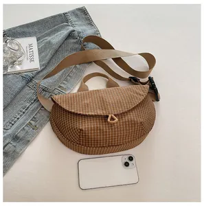 Vista detallada de un bolso bandolera de lona a cuadros marrones en un elegante flat lay