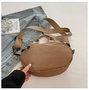 Bolso bandolera de lona marrón con patrón de rejilla blanca en un escenario de estilo de vida.