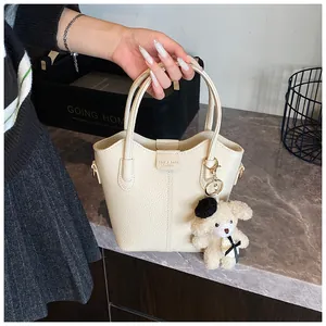 Elegant cream-colored textured leather bucket handbag featuring a cute plush bear pendant charm