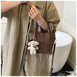 Brown pebble-grain bucket bag with teddy charm styled with a beige trench coat