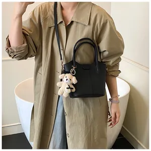 Chic black women's bucket bag with cute teddy bear charm shown on a trench coat model