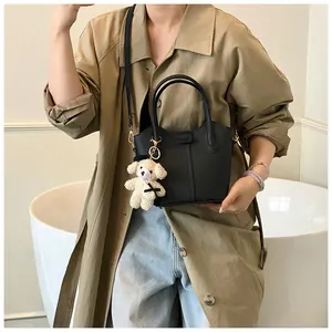 Minimalist black pebbled leather bucket bag with cute teddy bear charm for women.