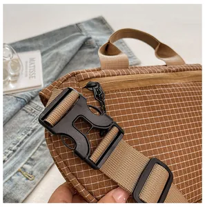 Detalle de la hebilla de plástico negro en el bolso de lona marrón con diseño de cuadros.