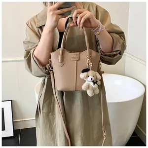 Close-up of beige pebbled leather bucket bag with cute teddy bear charm hanging.