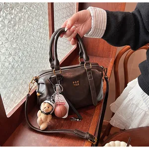 Schicke braune Vintage-Boston-Tasche mit Bärenanhänger in einem gemütlichen Café-Ambiente