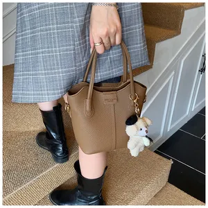Detailed view of a textured brown leather bucket bag with a stylish teddy bear charm
