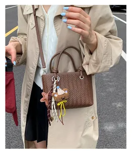 Braune geflochtene Handtasche mit Bärenanhänger, getragen von einem Modell