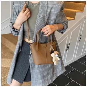 Brown leather bucket bag with cute bear charm worn by a model in a plaid blazer