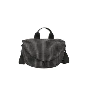 Detalle de bolso bandolera impermeable con patrón de cuadrícula negra y cierre magnético