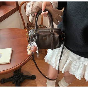 Detailansicht einer braunen Retro-Boston-Tasche mit stilvollen Anhängern und Logo.