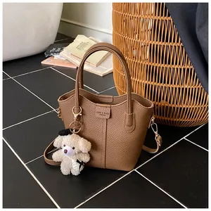 Close-up of brown pebbled leather bucket bag with cute teddy bear charm accessory for women