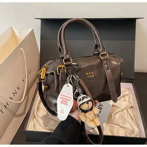 Detail der braunen Boston-Tasche mit Bären-Anhänger in Geschenkbox-Verpackung.