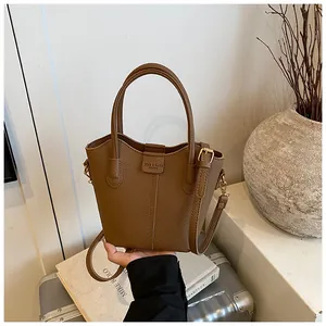 Macro view of a brown pebbled leather bucket bag being held against a minimalist background