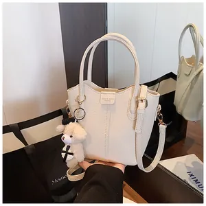 Chic cream textured leather bucket bag featuring a cute teddy bear plush charm detail