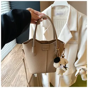 Close-up of a stylish light brown textured bucket bag with a cute dog keychain accessory