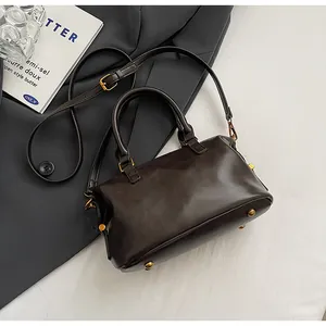 Detailansicht einer dunkelbraunen Boston-Handtasche mit goldfarbenen Metallfüßen.