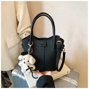 Black pebbled leather bucket handbag with a cute white bear keychain accessory.