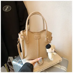 Close-up view of the beige textured bucket bag featuring a cute white teddy dog charm